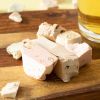 Gekleurde stukken haknougat met amandelen op een houten plank naast een glas thee