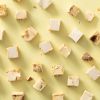 Losse blokjes soft nougat met kaneelamandelen verspreid over een lichtgele achtergrond