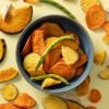 Kleurrijke groentechips in een donker schaaltje met losse chips eromheen