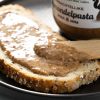 Close-up van amandelpasta op een snee brood met pot op de achtergrond