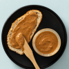Amandelpasta karamel zeezout op een snee brood met een houten spateltje en een geopend potje op een zwart bord