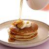Biologische ahornsiroop wordt over pannenkoeken met banaan geschonken