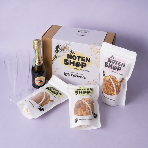 Let’s Celebrate box met prosecco, snackzakjes en glazen op een lichtpaarse achtergrond Let’s Celebrate box met prosecco, snackzakjes en glazen op een lichtpaarse achtergrond