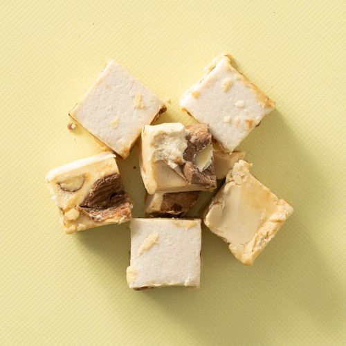 Blokjes soft nougat met kaneelamandelen op een lichtgele achtergrond Blokjes soft nougat met kaneelamandelen op een lichtgele achtergrond