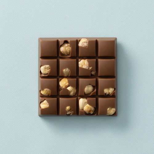 Melkchocolade choc block met stukjes hazelnoot op een lichtblauwe achtergrond Melkchocolade choc block met stukjes hazelnoot op een lichtblauwe achtergrond