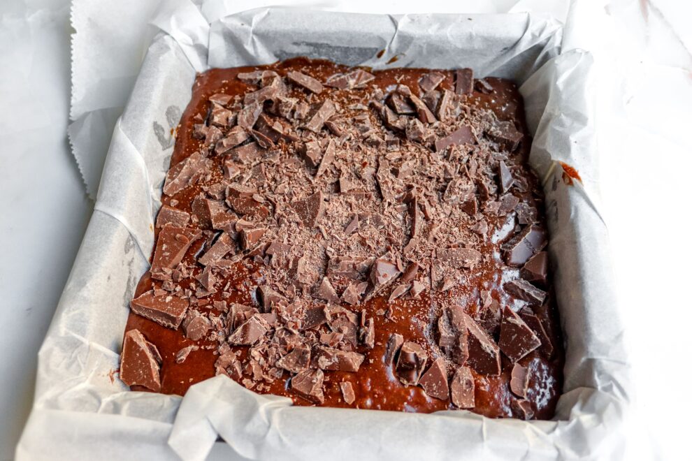 Browniebeslag met stukjes chocolade erover in een grote vierkante bakvorm